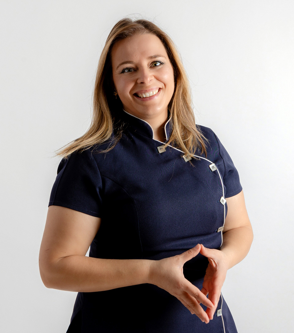 Nádia Neto. Sorridente e acolhedora, com cabelo louro e olhos verdes, Nádia Neto é uma terapeuta holística apaixonada por ajudar os outros a encontrar equilíbrio e bem-estar. Ela está vestida de forma casual e profissional, refletindo sua abordagem amigável e acessível.